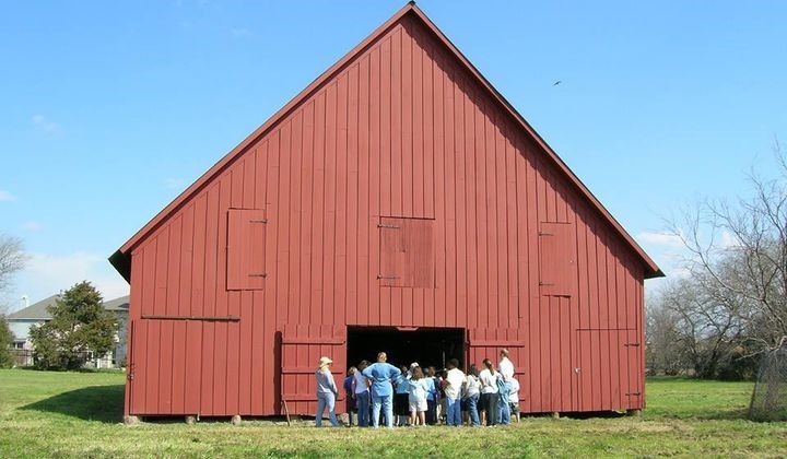 A bright red-painted Pennsylvania Dutch barn with a group of people standing in front of the barn door.. 