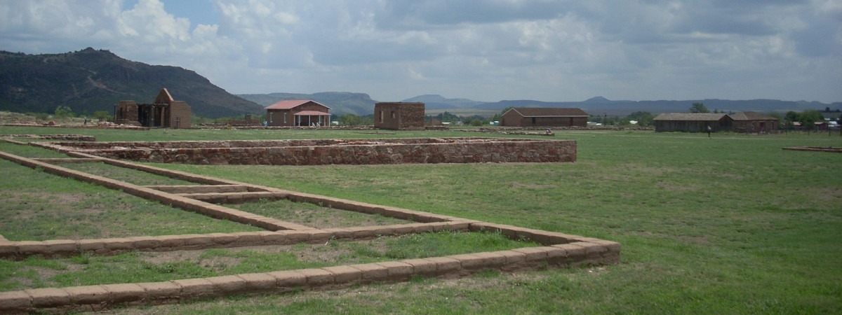 A landscape view of Fort Davis National Historic Site, with low, linear shapes of adobe foundations in the foreground and adobe structures in the middle ground, and mountain in the background.