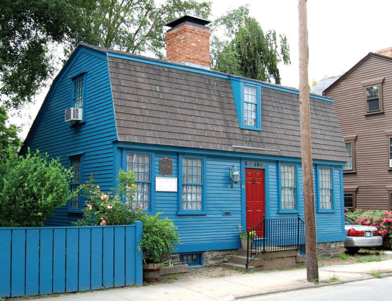 A small historic house painted bright blue with a red door.