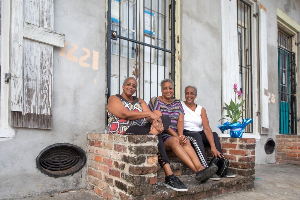 Three sisters sitting on the red brick front steps of their white-stuccoed home in New Orleans.