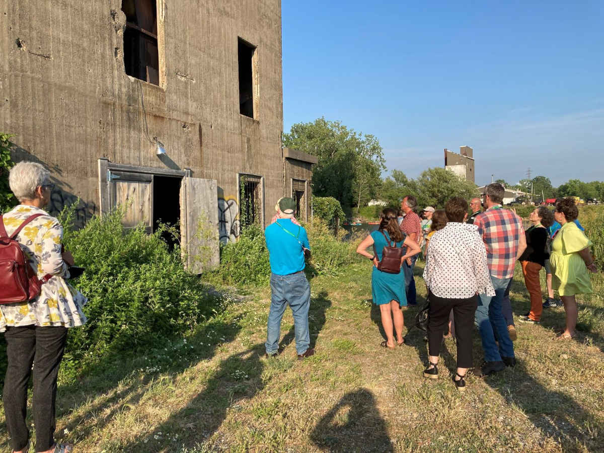 A group of people with their backs to the camera are standing in front of a vacant former grain silo in Buffalo, NY.