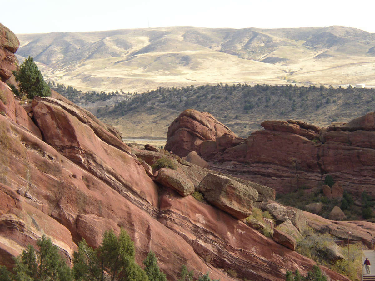 A landscape view taken at Red Rocks Park outside of Denver, CO, showing sedimentary rocks in the foreground and treeless hills in the background.