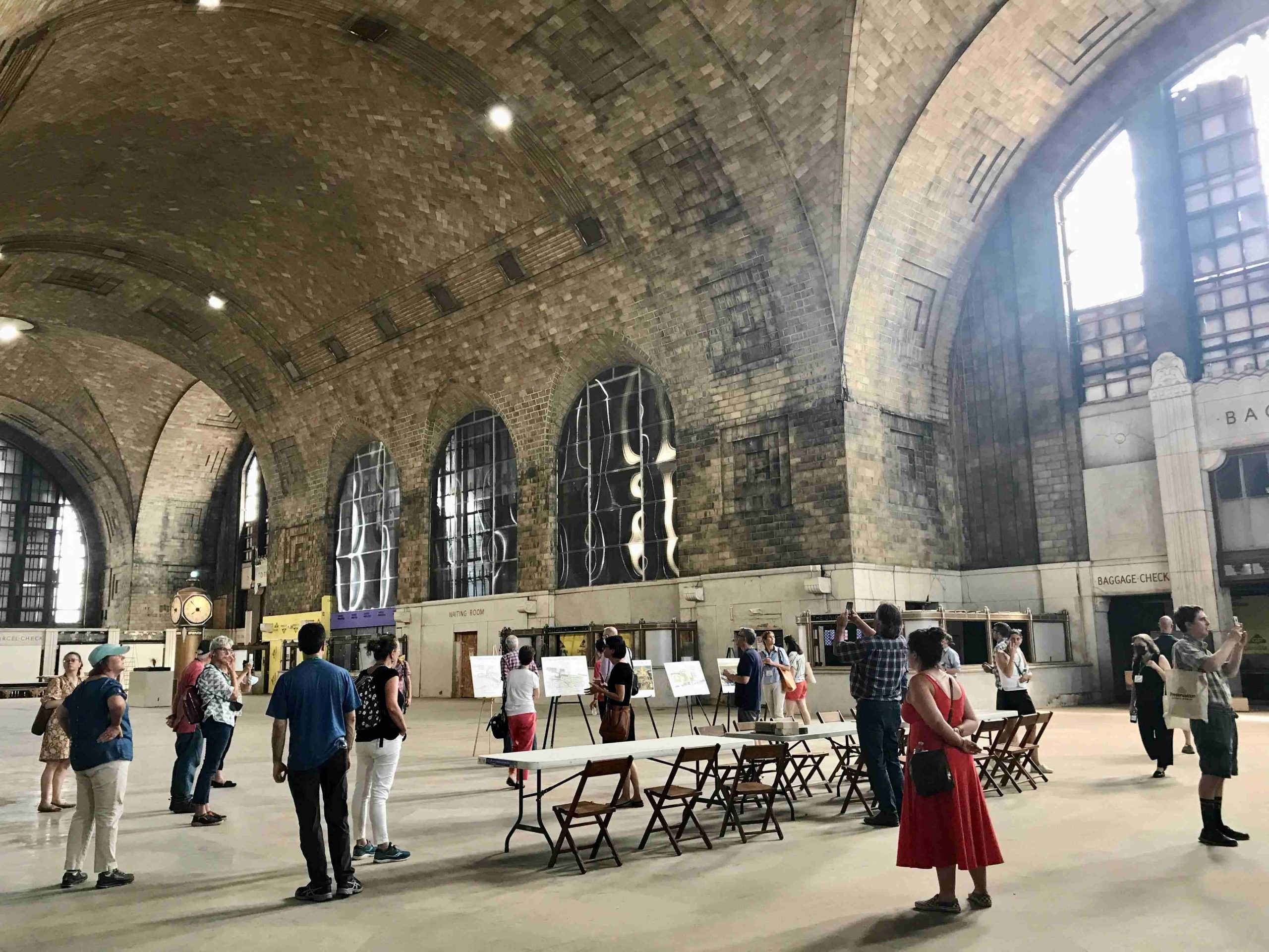 Vaulted interior of a former train station in Buffalo, NY. People are milling around looking at plans for the site's reuse. 